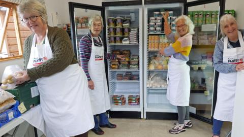 Volunteers from the West Somerset Food Cupboard are stood in front of a fridge fully stocked with produce