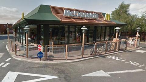 Google image of the MacDonald's restaurant on Cottingham Road in Hull. It is a modern-looking building with the letters of the company name and yellow logo on its roof. The building is surrounded by railings, with parking and white markings on the perimeter road.