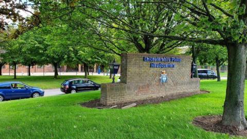 A photograph outside of Leicestershire Police Headquarters showing a wall with the force's name on and cars parked in the background