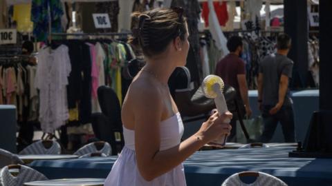 A woman cools herself with a handheld electric fan