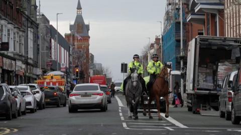 Two police horses patrolling along a busy high street