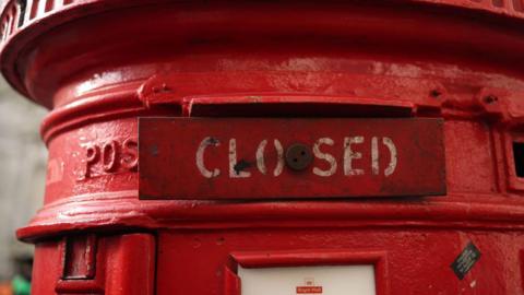 A red post box. The opening has been blocked with a piece of metal that reads "closed".