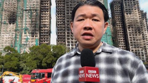 BBC reporter in front of Hong Kong buildings damaged by fire