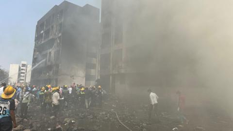 Rescue team members work as smoke rise at the crash site where an Air India plane crashed in Ahmedabad, India