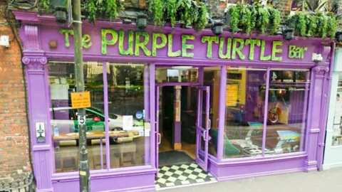 The Purple Turtle Bar and Music venue, is a red brick building with a purple frontage.