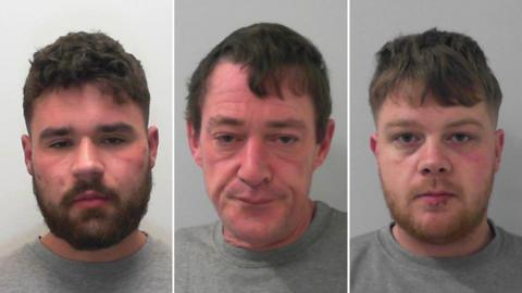 Side-by-side mugshots of three criminals, all of whom are wearing grey sweaters. The men at the sides are in their twenties with short beards and the man in the middle is aged around 50. He has short hair