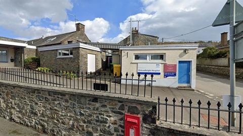 A flat-roofed hospital building in Kirkcudbright with a sign outside and a low stone wall in front with spiked railings