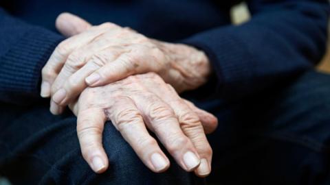 Older person's hands resting on their lap