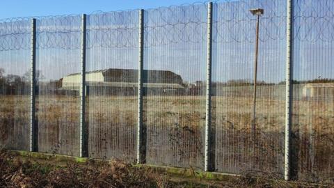 A prison fence in front of a large prison building