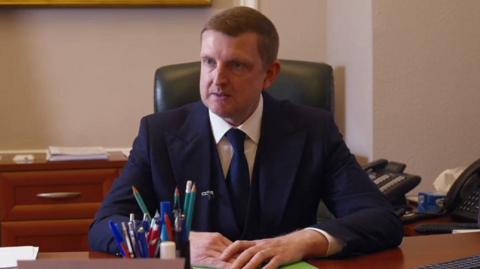 Ihor Brusylo, sat in a suit behind a desk with papers and pencils on it