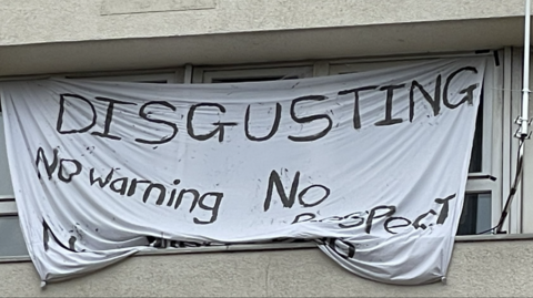 A white sheet hung up across a window in Barton House in Bristol, with painted words reading: "Disgusting, no warning, no respect"