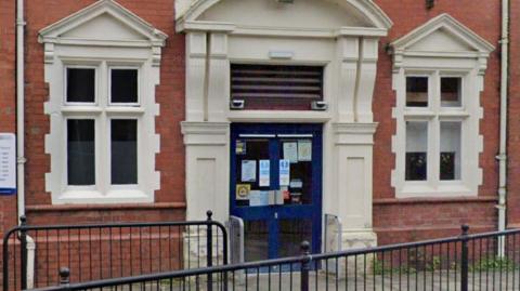 The entrance to a red brick building with a large blue door in a white frame and black railings in front of it