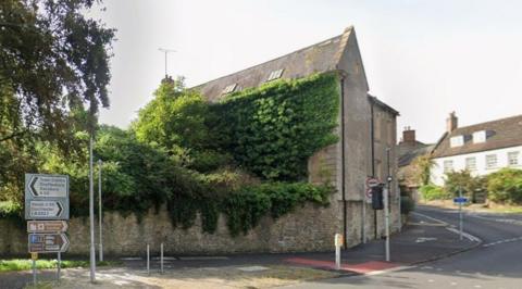 The grey building on a road corner, with ivy growing on the full front and on to part of the roof