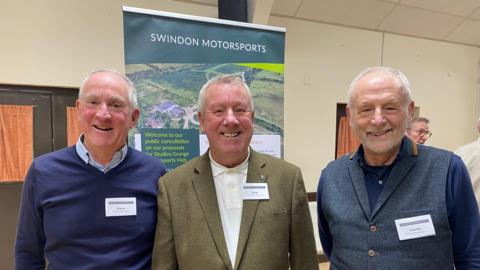 Steve Park, Terry Russell and Clarke Osborne - all involved in the scheme -  are standing in a hall in front of a banner with the plans. They are all smiling and looking into the camera. All are dressed smartly in shirts with name tags.