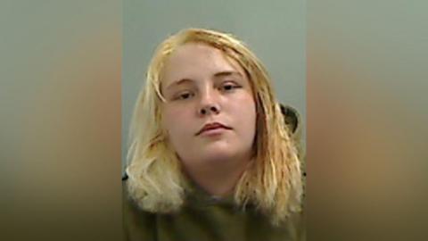 Mugshot of Cerr. She has blonde hair and is wearing a green hoody