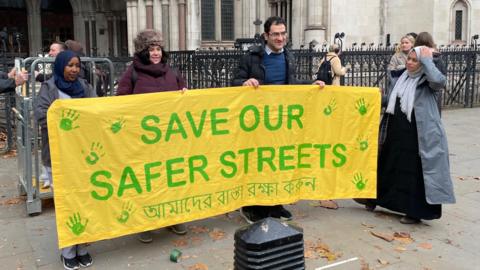 Four people holding a yellow sign which says save our safer streets in green.