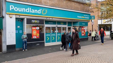 A Poundland store with people walking past on a paved street