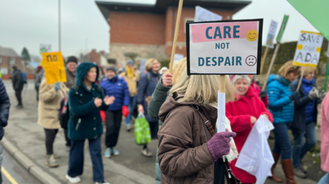 Campaigners holding placards and marching through the streets of Belper. Placards read "Care not despair" and "Save our Ada"