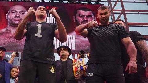 Tyson Fury puts up his fists as Arslanbek Makhmudov points to the camera