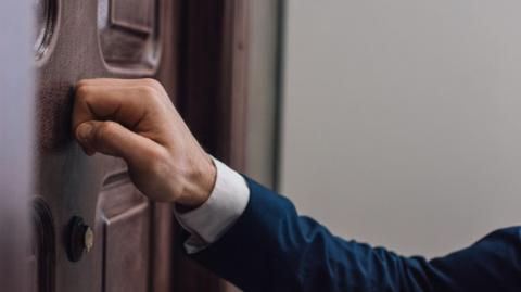 A suited man's arm, knocking on a house door