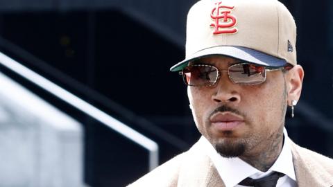 Chris Brown in beige suit and with cap and glasses outside court