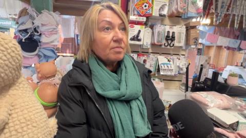 A blond woman in a black coat and green scarf