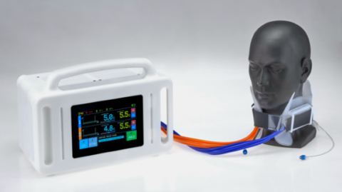 This appears to be a design image of the collar set against a white background. On the right is a dark grey model of a human head and neck, wearing the collar. It has two brightly coloured cables (one orange, the other blue) connecting it to a small white machine that looks like a digital radio. The machine has a black screen on the front which displays digits 5.0c, 4.8c and 5.5c along with plus and minus signs in boxes.