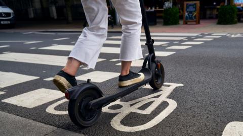 A person rides a black e-scooter in a cycle lane. 