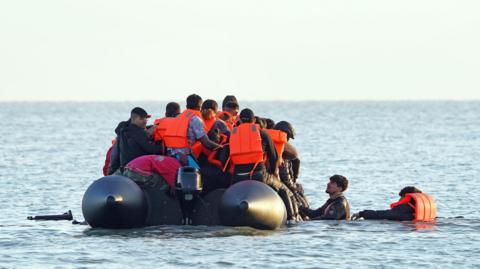 A group of people thought to be migrants wade through the sea to clamber aboard a small boat off the beach in Gravelines, France