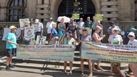 A large group of people stand on steps outside Sheffield City Hall holding banners and placards