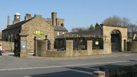 Light coloured brick mill buildings with a sign that reads: Bradford Industrial Museum