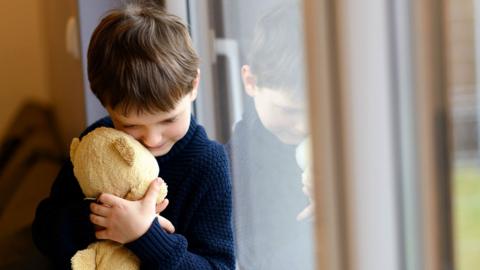 Young boy holding teddy next to window