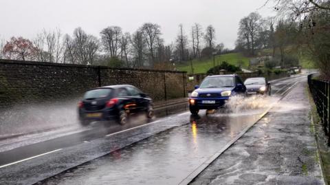 A photo of cars driving through large puddles on a road