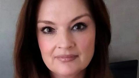 A headshot of Fiona Drouet. She has brown hair and is smiling. She is wearing dark eye makeup.