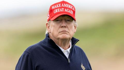 Donald Trump wearing a Make America Great Again hat and blue golf jumper