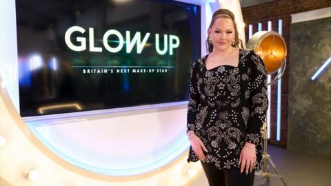 NikkieTutorials is standing in front of a screen that has the words 'Glow Up'