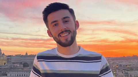 Llion Wright-Evans in a holiday snap smiles with a background of a beautiful orange sunset and a city skyline