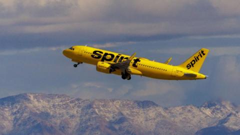 A yellow Spirit Airlines plane flying over a mountain range.