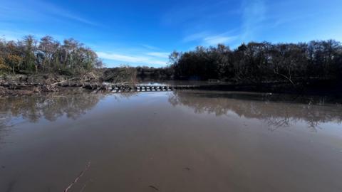 A flooded pathway that looks like it could be a river with trees surrounded it and a crater looking path above it.