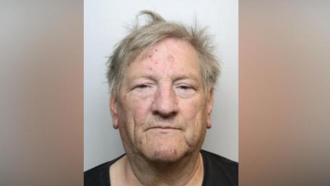 A police mugshot of Christopher Wright. Wright is facing directly toward the camera. He has short, light-coloured hair that appears slightly tousled. Several small red marks are visible on the forehead, and another red mark is visible on the chin. The eyes are partially open, and the face is evenly lit. He is wearing a dark-coloured top, of which only the upper neckline and shoulders are visible.