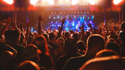 A large crowd, some people with hands in the air, in front of a stage with blue lights shining down on the people on stage.