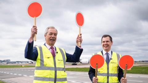 Reform UK leader Nigel Farage and Treasury spokesman Robert Jenrick pictured in hi-viz jackets on a runway at Heathrow Airport