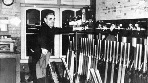 A black and white image of a man in a signal box pulling levers