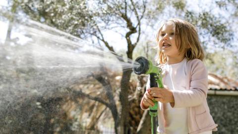 a girl holding a hosepipe with a nozzle in a garden spraying water