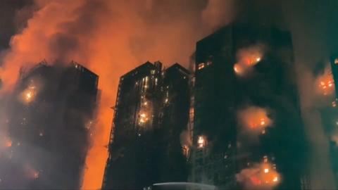 At night flames and bright red smoke engulf black tower blocks
