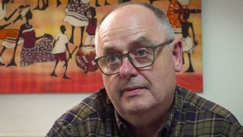 Geraint Rees yn gwisgo sbectol ac yn edrych yn ei flaen.