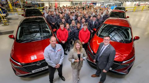 Kim McGuinness standing in front of workers at Nissan's plant in Sundelrand. Red Nissan cars are parked on either side of the crowd.