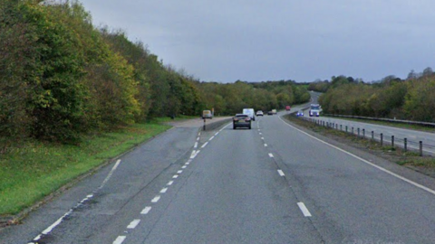 A two lane A-road, with some cars travelling along it, and a layby to the side