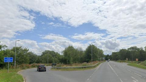 A Google street view of the A1034 slip road onto the A63 near South cave showing metal crash barriers surrounded by trees