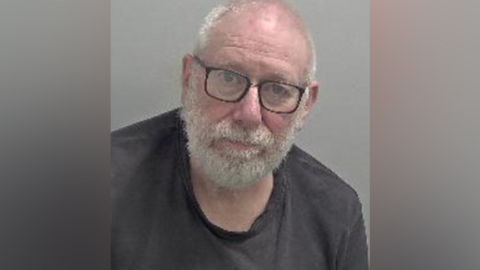 A police mugshot of a man with glasses looking into the camera.